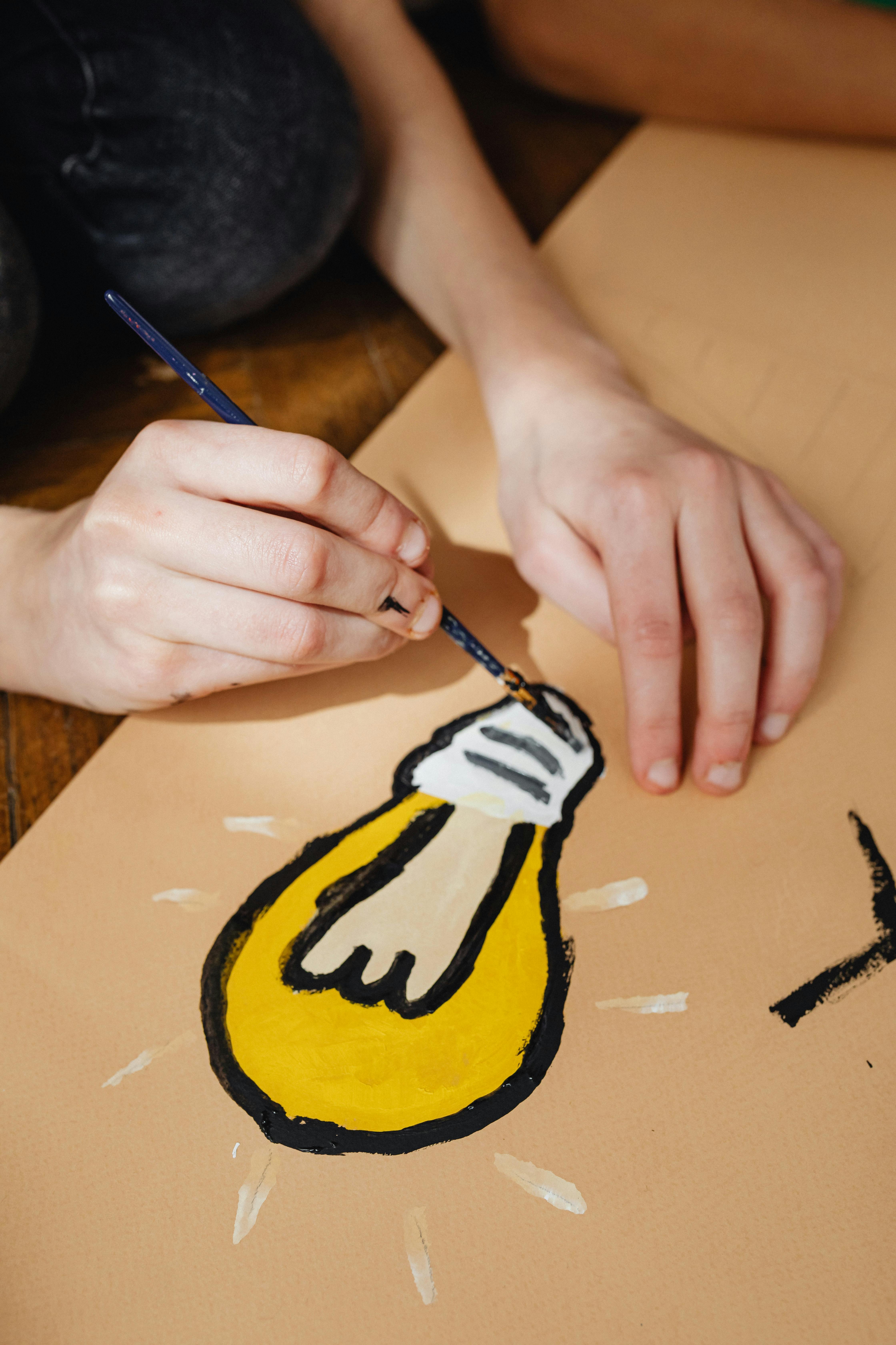 Conseil stratégique et gestion de projets innovants pour la petite enfance avec finidoo. Main peignant une ampoule symbolisant la créativité, illustrant les services de conseil et gestion de projets de finidoo pour les institutions de la petite enfance.