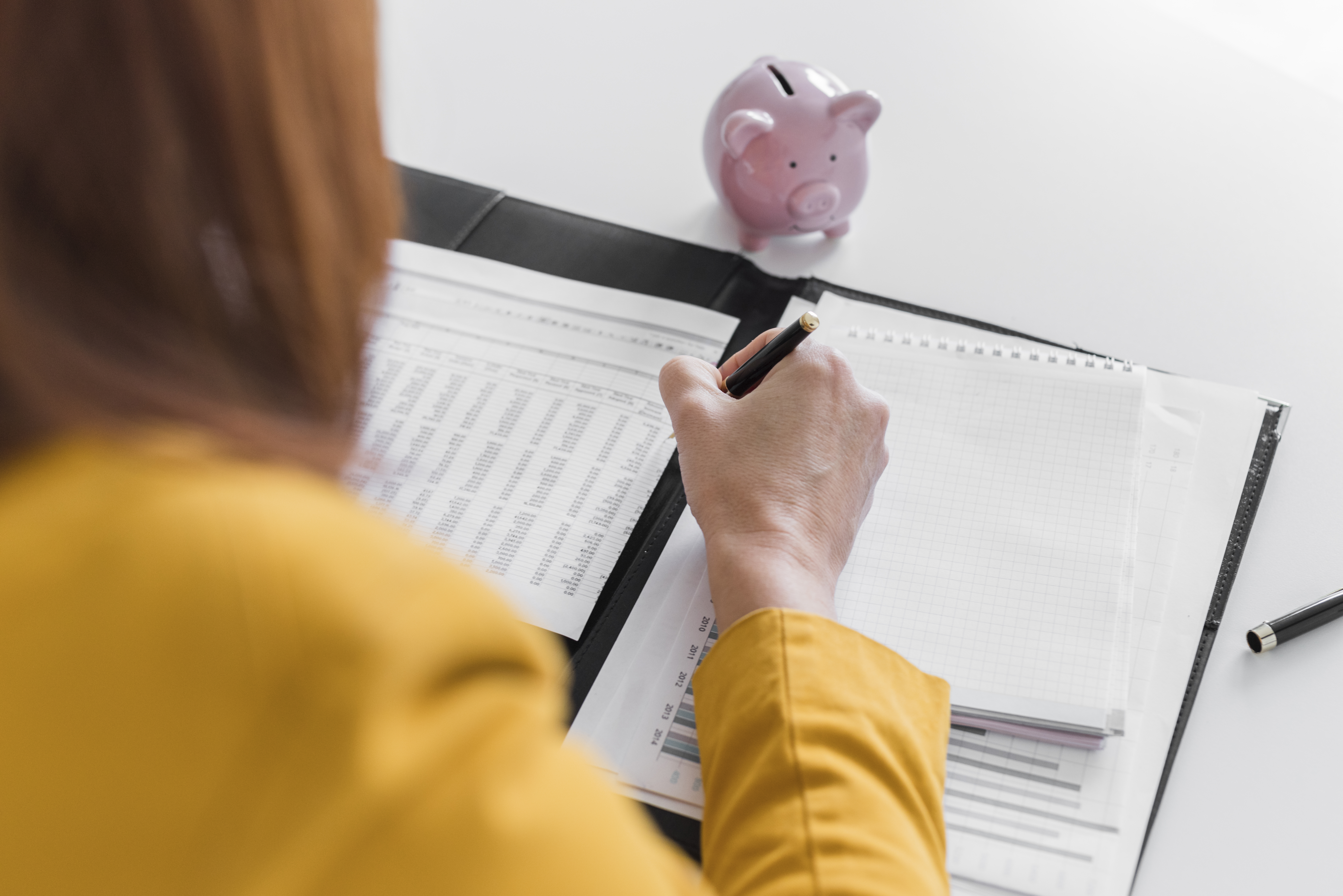 Gestion professionnelle des salaires pour les structures d’accueil de la petite enfance avec finidoo. Personne travaillant sur des documents financiers avec une tirelire rose, illustrant la gestion des salaires proposée par finidoo pour les institutions de la petite enfance.